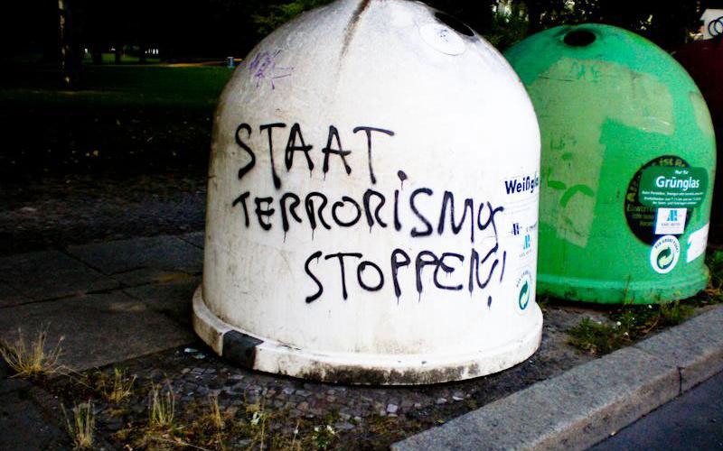 Glaßmülltonne mit der Aufschrift "Staat Terrorismus Stoppen"