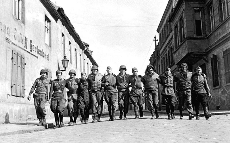 Amerikanische und sowjetische Soldaten laufen Arm in Arm in einer Reihe auf einer Straße im deutschen Torgau