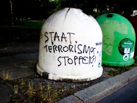 Glaßmülltonne mit der Aufschrift "Staat Terrorismus Stoppen"