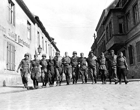 Amerikanische und sowjetische Soldaten laufen Arm in Arm in einer Reihe auf einer Straße im deutschen Torgau