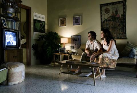 Avner Kaufman (Eric Bana) und Daphna Kaufman (Ayelet Zurer) sitzen vor dem Fernsehen