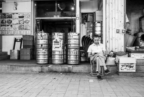 Schwarzweißfoto eines vor einem Biergeschäft sitzenden Mannes in Qingdao