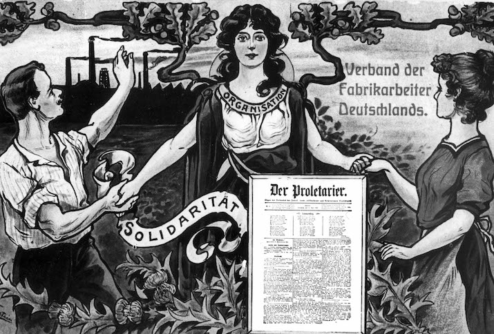 Das Motiv entstand 1909 und zeigt Arbeiterin und Arbeiter sich in Solidarität die Hände reichend. Im Hintergrund rauchen die Fabrikschlote, im Vordergrund ist die Titelseite der Zeitung "Der Proletarier" abgebildet