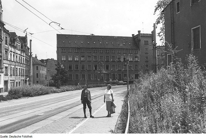 Schwarz-weiße Fotografie von einem älteren Ehepaar, das auf einer Straße vor einem verlassenen Gebäude steht